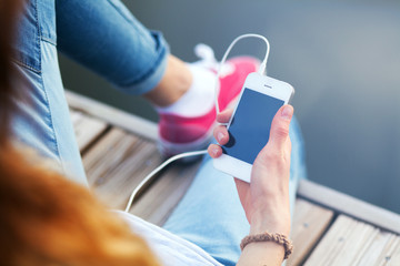 Young woman sitting on pier holding a smartphone