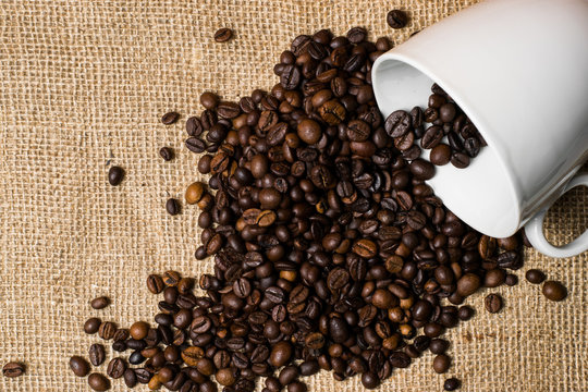 Cup full of coffee beans spilled over cloth background