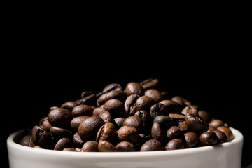 Coffee mug filled with coffee beans over black background