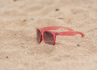 Pink sunglasses left on a sandy beach