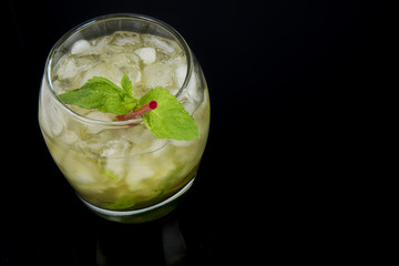A Mint Julep, the official drink of the Kentucky Derby, with fresh mint leaves, crushed ice, and a red stir stick with a black background. Drink is oriented on the left side of the photo.