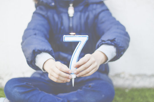 Girl sitting cross legged holding a number seven candle