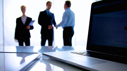 Laptop  computer on  desk , three businesspeople standing in the