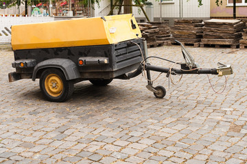Ein gelber fahrbarer Kompressor parkt auf Kopfsteinpflaster