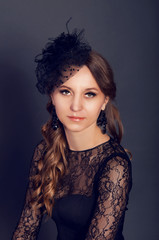 Fototapeta premium Elegant young woman in black lace dress and veil hat with long c