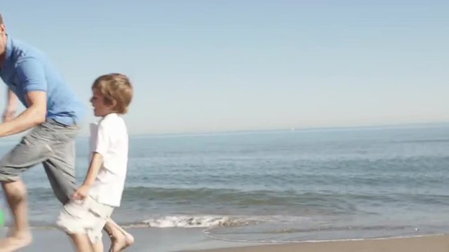 Family chasing beach ball along beach
