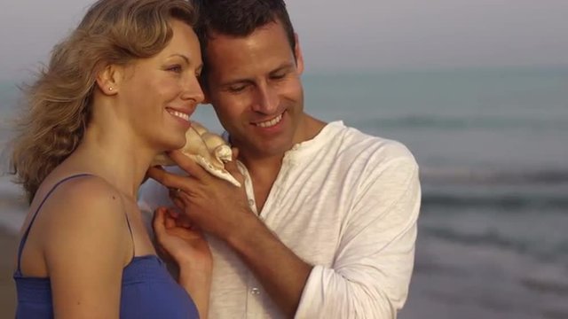 Couple listening to conch shell by sea. 