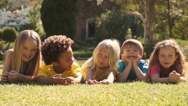 Five children lying on grass in park looking at camera.