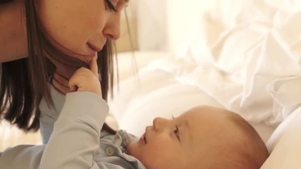 Mother and 12 month old baby  playing on bed indoors.