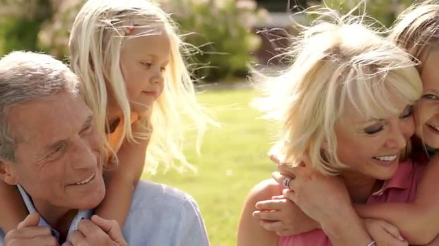 Grandparents and two granddaughters playing in park, hugging together.