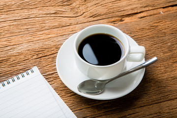 Hot black coffee with blank note book on wood table.