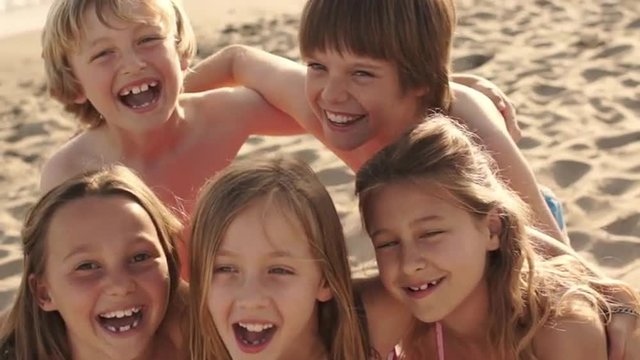 Close up of five children on beach facing camera and laughing.