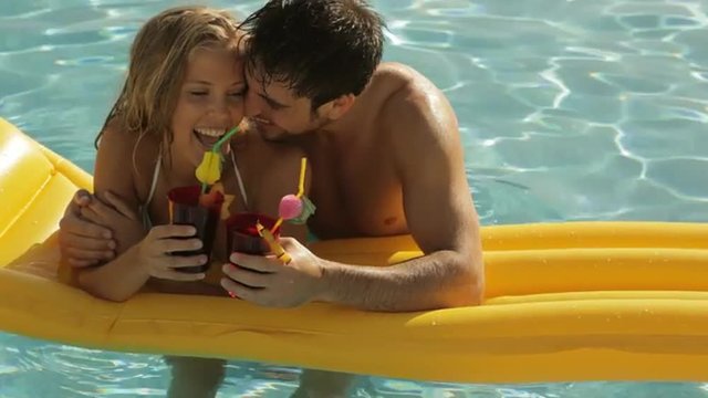 young couple playing and laughing on lilo in pool