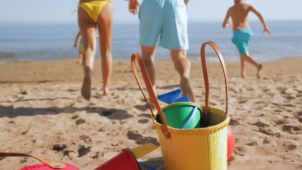 family dropping bags and running down beach to sea - Powered by Adobe
