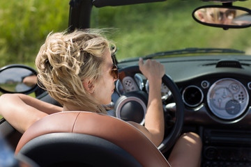 Blonde woman drives cabrio car, in summer sunshine