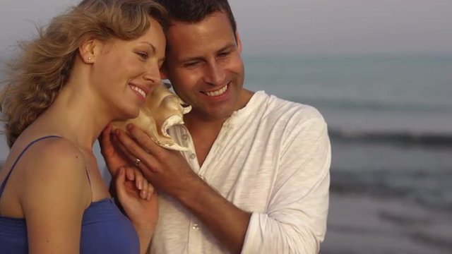 Couple listening to conch shell by sea.