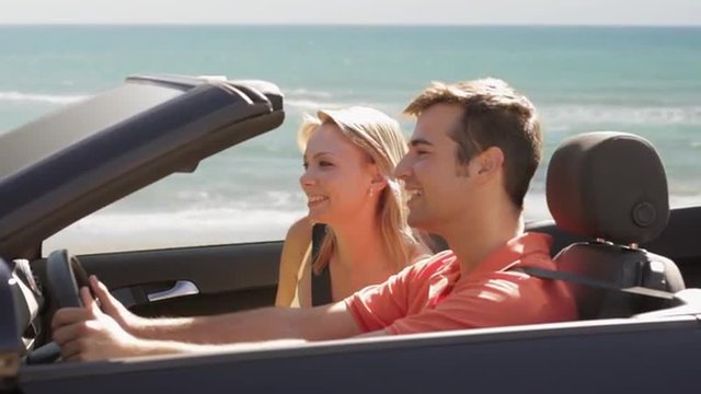 young couple driving convertible car by beach