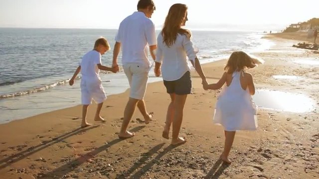 Pan Shot Of Family Walking Away From Camera On Beach