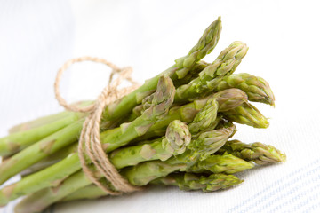 Asparagus Bundle Tied with Twine – A bunch of asparagus spears are tied in a bundle with twine. On a light blue and white background.