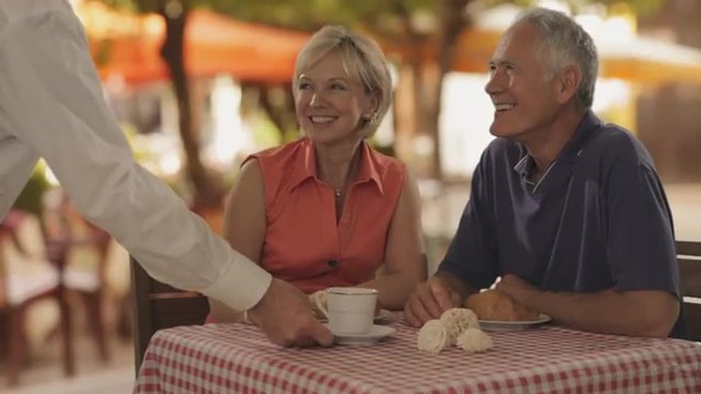 senior couple at cafe in town waiter bringing coffee