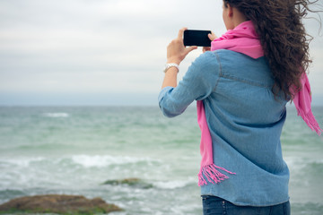 Young woman with curly hair in denim clothes takes a picture of