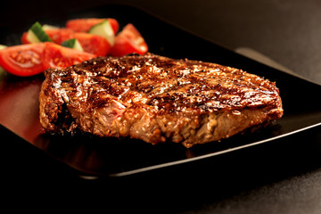 Grilled steak and vegetables on black plate macro