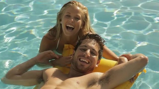 young couple playing and laughing on lilo in pool