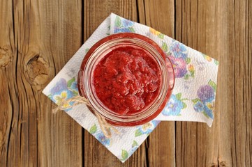 Homemade strawberry jam in open glass jar with hempstring on pap