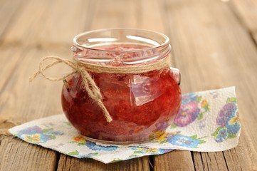 Homemade strawberry jam in open glass jar with hempstring on pap