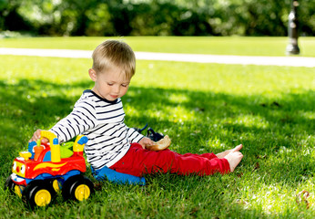 Little preschool boy playing with big toy car at city park