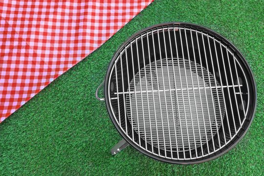 Red Picnic Tablecloth And BBQ Grill Appliance On The Lawn