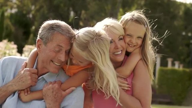 Grandparents and two granddaughters playing in park, running to grandparents.