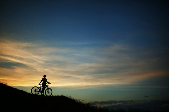 Silhouette of tourist and bike on sky background.