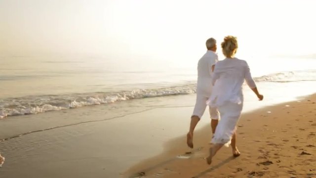pan shot of senior couple running on beach
