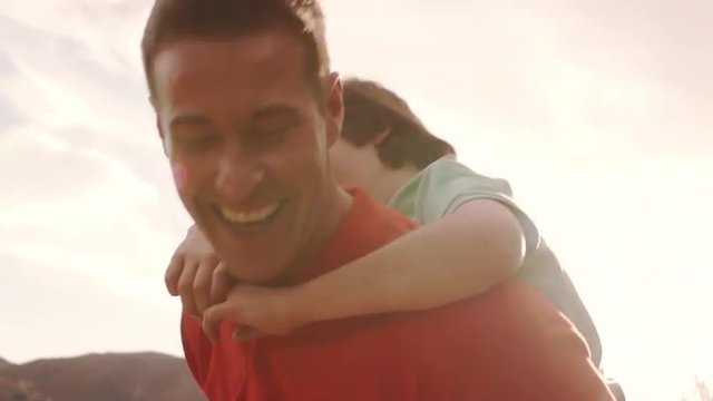 Slow motion of father with son on back playing in countryside.