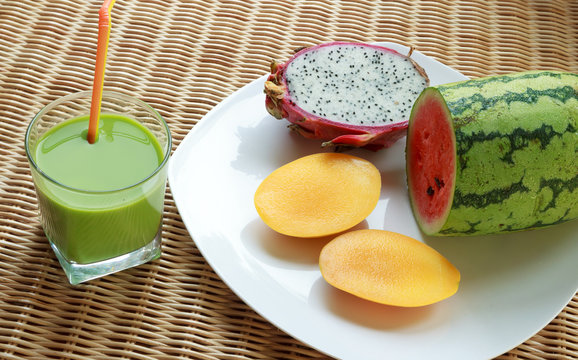 Blended green smoothie and sliced tropical fruits