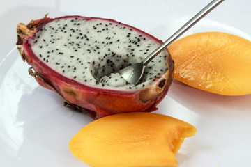 Dragon fruit and mango sliced on white plate with spoon