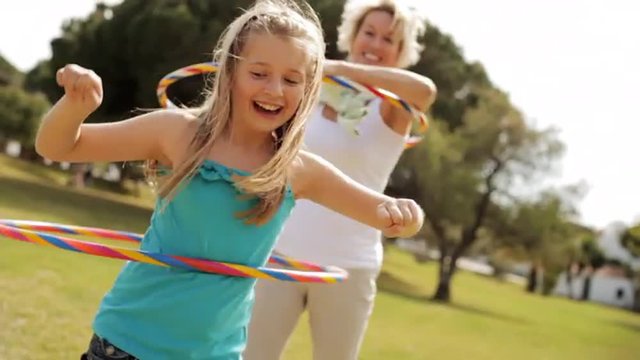 Grandmother and granddaughter playing with hula hoops in park.