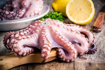 whole fresh raw octopus  on cutting board with lemon