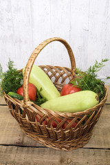 fresh vegetables, cucumbers, squash, tomatoes and fennel in a wicker basket on wooden background