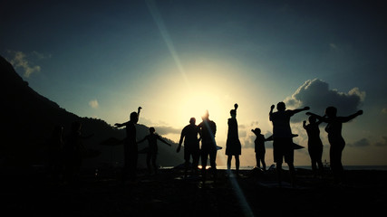 Silhouette of people doing Yoga at sea coast sunrise time