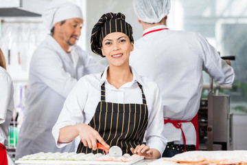 Happy Chef Cutting Ravioli Pasta With Colleagues In Background