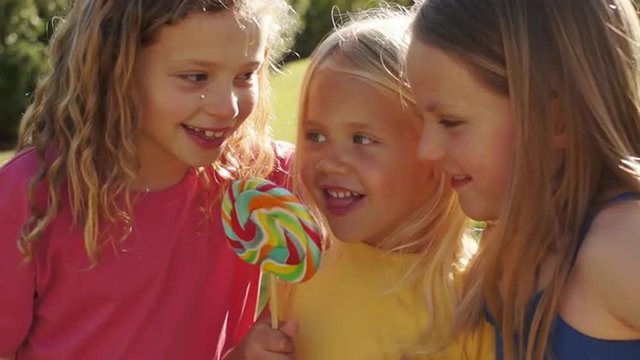 Portrait of three children licking lollypop in park.