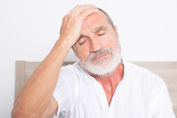 Obraz premium Elderly man sitting on bed suffering from headache