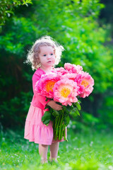 Little girl with peony flowers in the garden