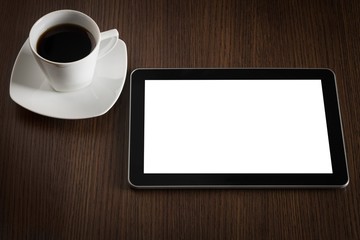 Fototapeta na wymiar Modern digital tablet with black screen and cap of coffee on dark wooden office desk.