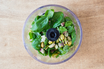 Ingredients for Pesto Sauce with Pistachio Nuts in a Plastic Bowl of Food Processor on Rustic Wooden Background