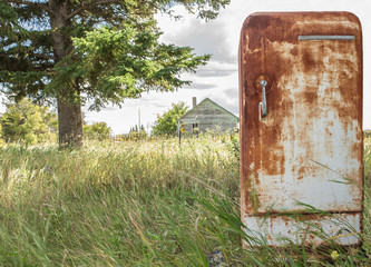horizontal image of an very old rusted fridge sitting outside in the grass in the summer time.