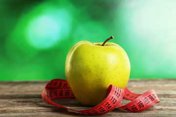Green apple with measuring tape on grey wooden background