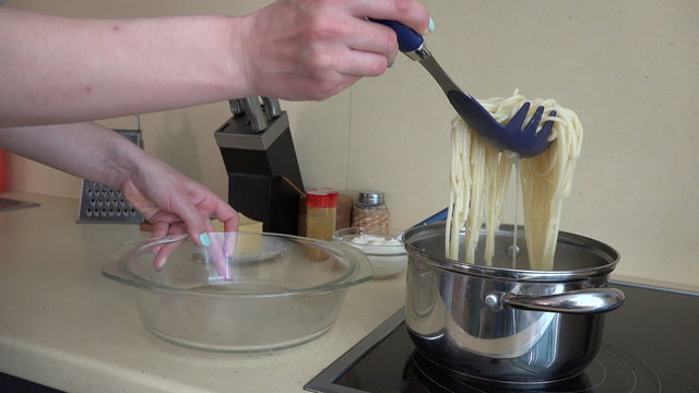 female hands take prepared spaghetti from pot to glass dish. 4K